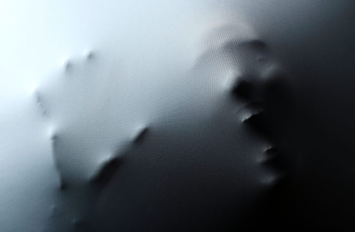 Screaming human face with hand pressing through fabric as horror background HORROR FILM