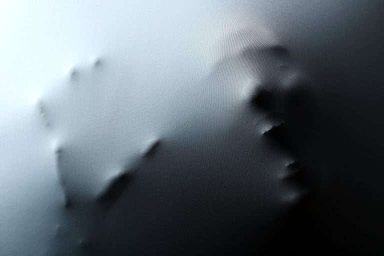 Screaming human face with hand pressing through fabric as horror background HORROR FILM