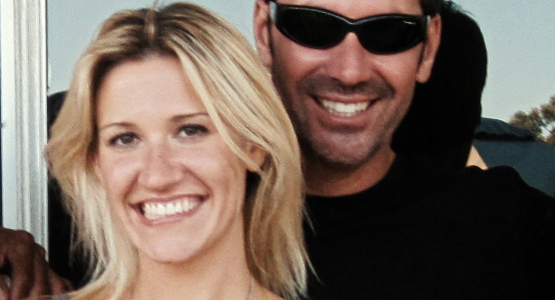"Smiling woman with blonde hair and a man in sunglasses standing close together outdoors, both appearing happy with sunlight and greenery in the background."