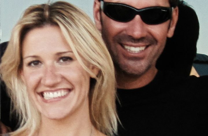 "Smiling woman with blonde hair and a man in sunglasses standing close together outdoors, both appearing happy with sunlight and greenery in the background."
